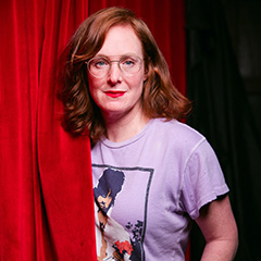 Jess Salomon, coming out from behind a theatrical red curtain