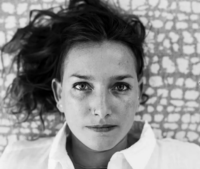 A black and white photo of Carly Thomas head and shoulders in a white collared shirt, lying on her back looking directly at the camera.